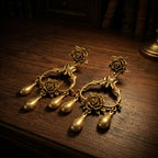 Vintage-inspired gold rose statement earrings resting on dark wood, showing intricate floral craftsmanship.
