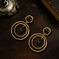 Vintage style heavy gold-plated earrings with black cabochons resting on dark wood, dark academia jewelry.
