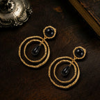 Vintage style heavy gold-plated earrings with black cabochons resting on dark wood, dark academia jewelry.