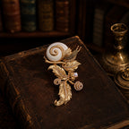 Vintage-style heavy gold snail and leaf brooch resting on an antique book, dark academia aesthetic.