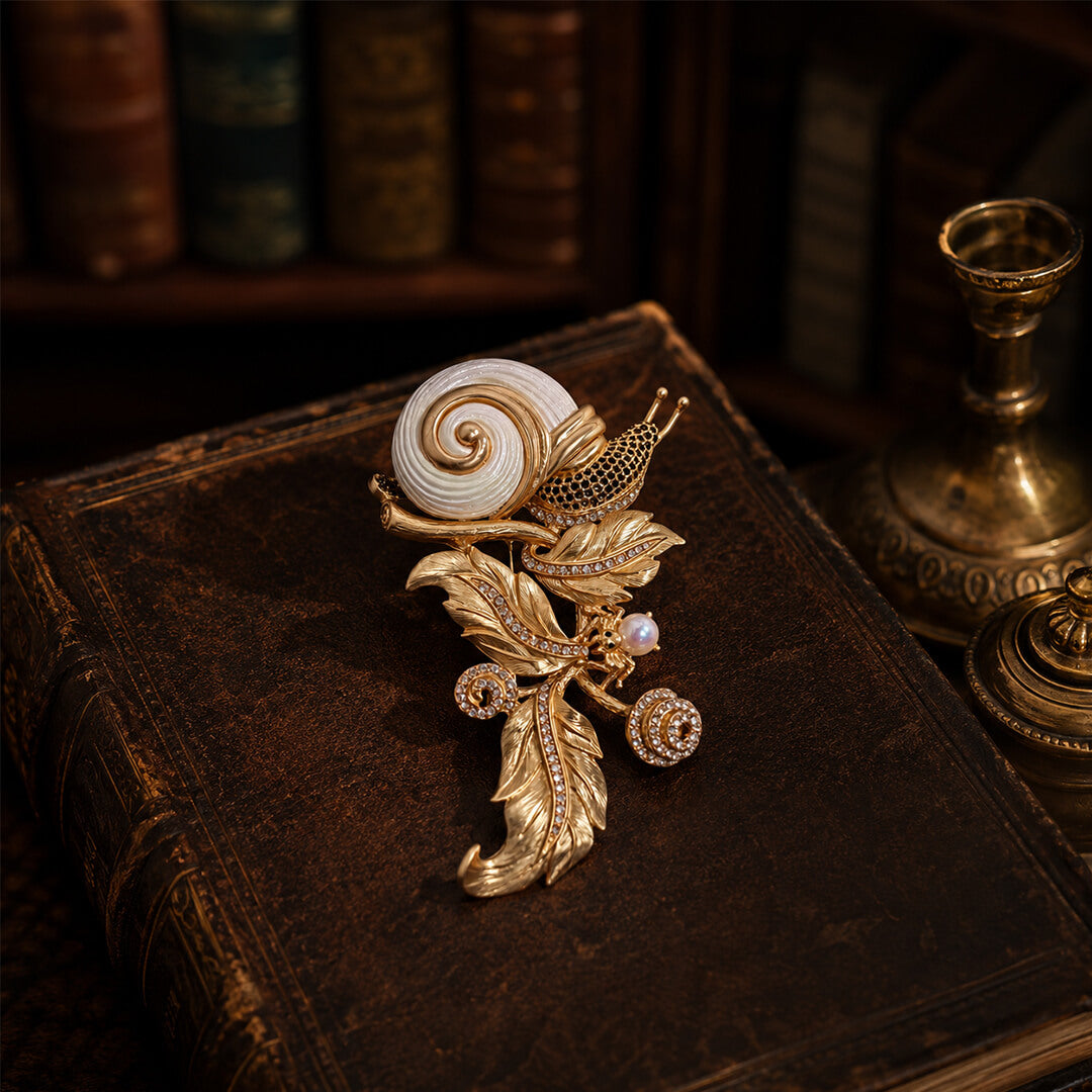 Vintage-style heavy gold snail and leaf brooch resting on an antique book, dark academia aesthetic.
