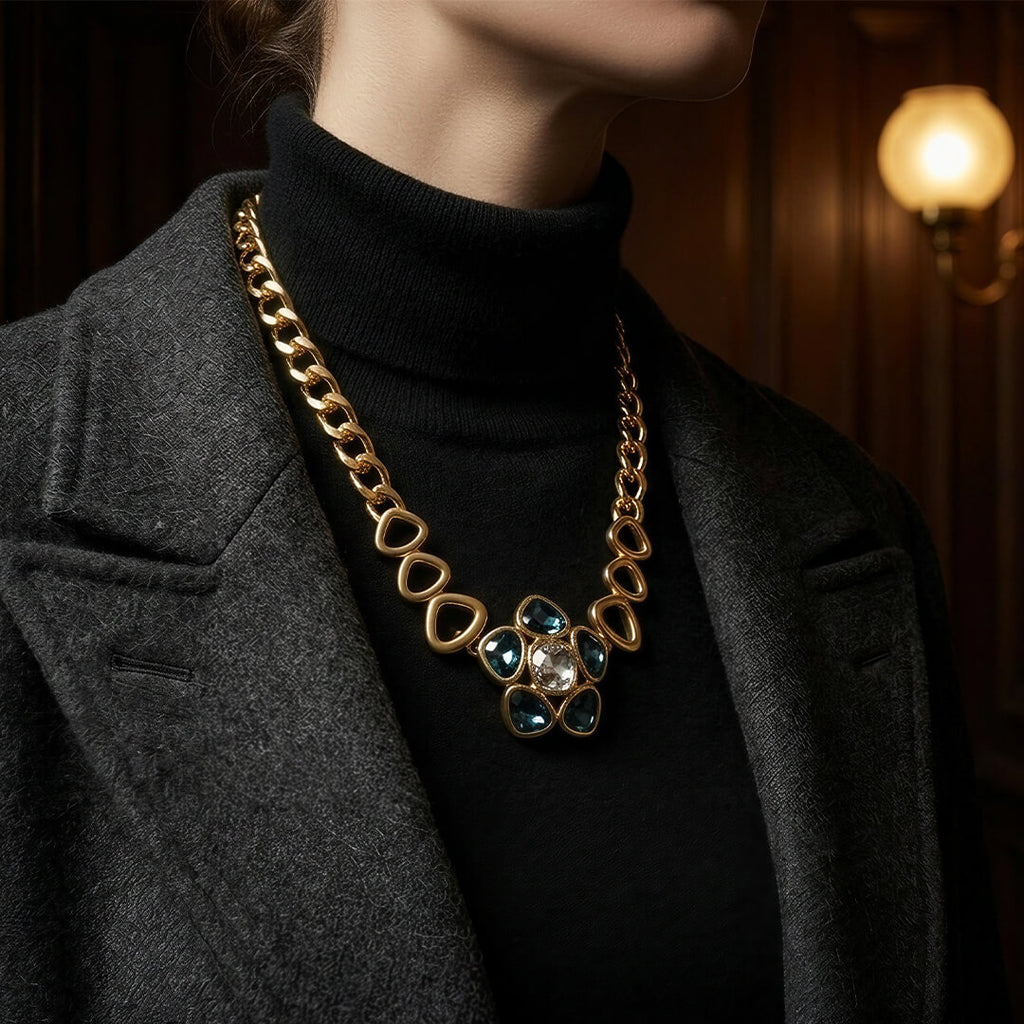 Alt Text: Close-up of a woman in a black turtleneck wearing a substantial vintage-inspired gold chain necklace featuring dark blue crystals.