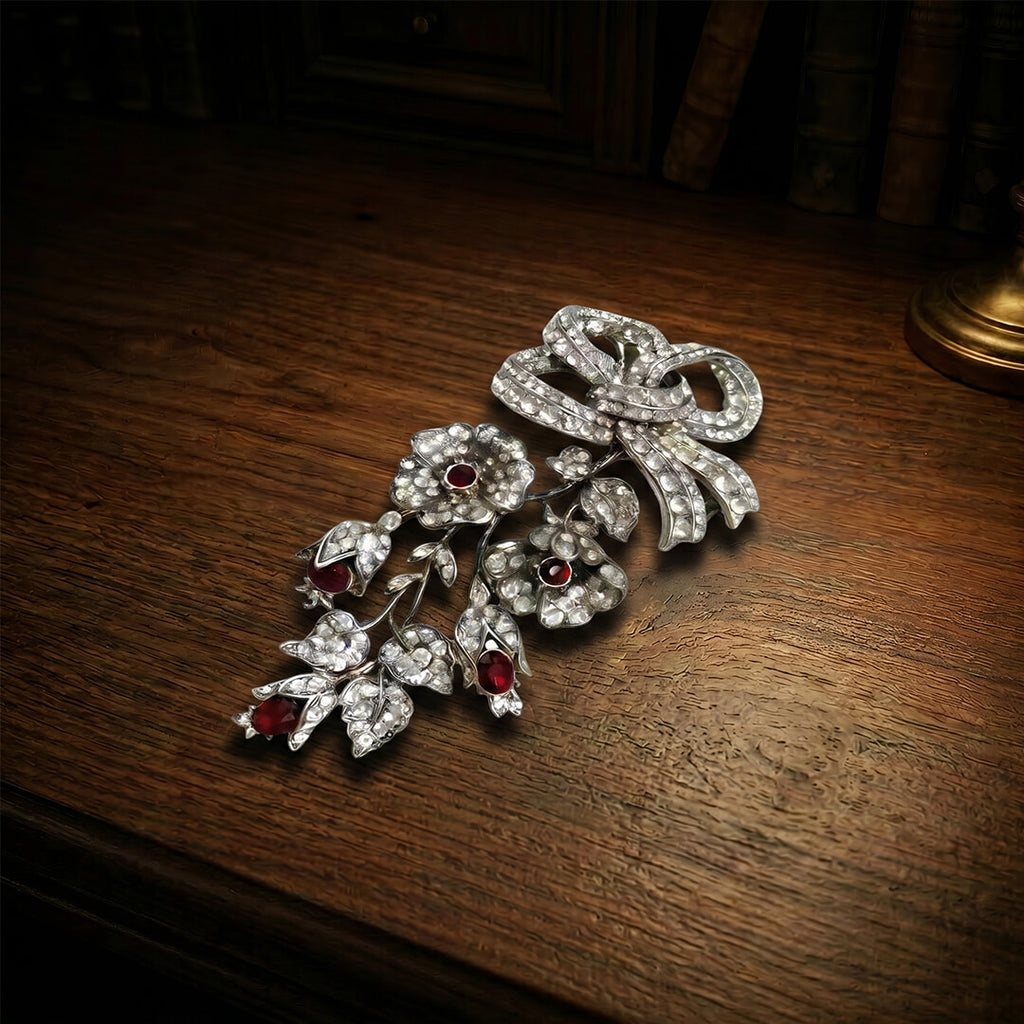 Heirloom quality Victorian revival bow brooch with deep red teardrop stones resting on a dark antique wooden desk.