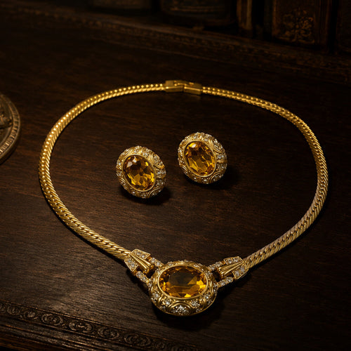 Main product image of Duskcast Imperial Citrine Set featuring a 1980s-inspired gilded choker necklace and matching oval amber earrings on a dark wooden table.