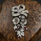 Duskcast Empress Bow vintage silver brooch with deep ruby zircons on a dark wooden background.