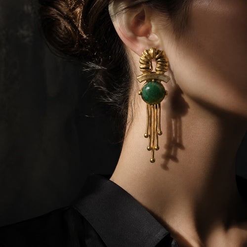 Elegant woman wearing 1980s retro style gold ribbed emerald drop earrings