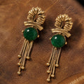 Vintage-inspired emerald green cabochon gold fringe earrings on dark leather