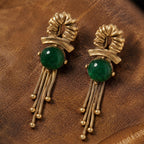 Vintage-inspired emerald green cabochon gold fringe earrings on dark leather