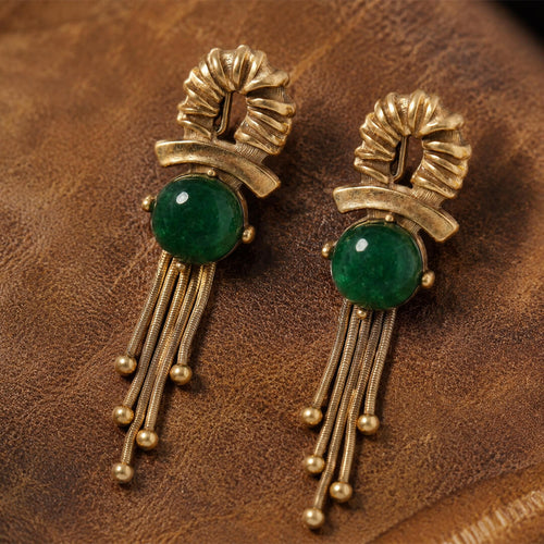 Vintage-inspired emerald green cabochon gold fringe earrings on dark leather