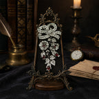The Empress Bow vintage-inspired silver and ruby-hued crystal statement brooch displayed on an antique bronze easel.