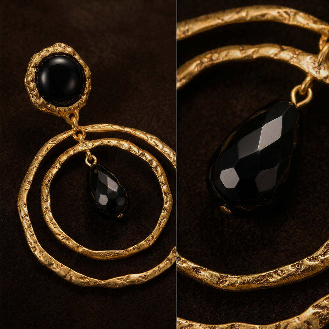 Close up of textured gold double hoop earrings featuring a faceted black teardrop stone.