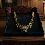 Alt Text: A vintage-inspired heavy gold-tone statement necklace with a blue floral geometric pendant resting elegantly inside a black velvet display tray.