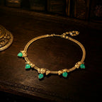 Vintage-inspired gold ivy leaf necklace with green resin stones resting on a dark wood antique desk.
