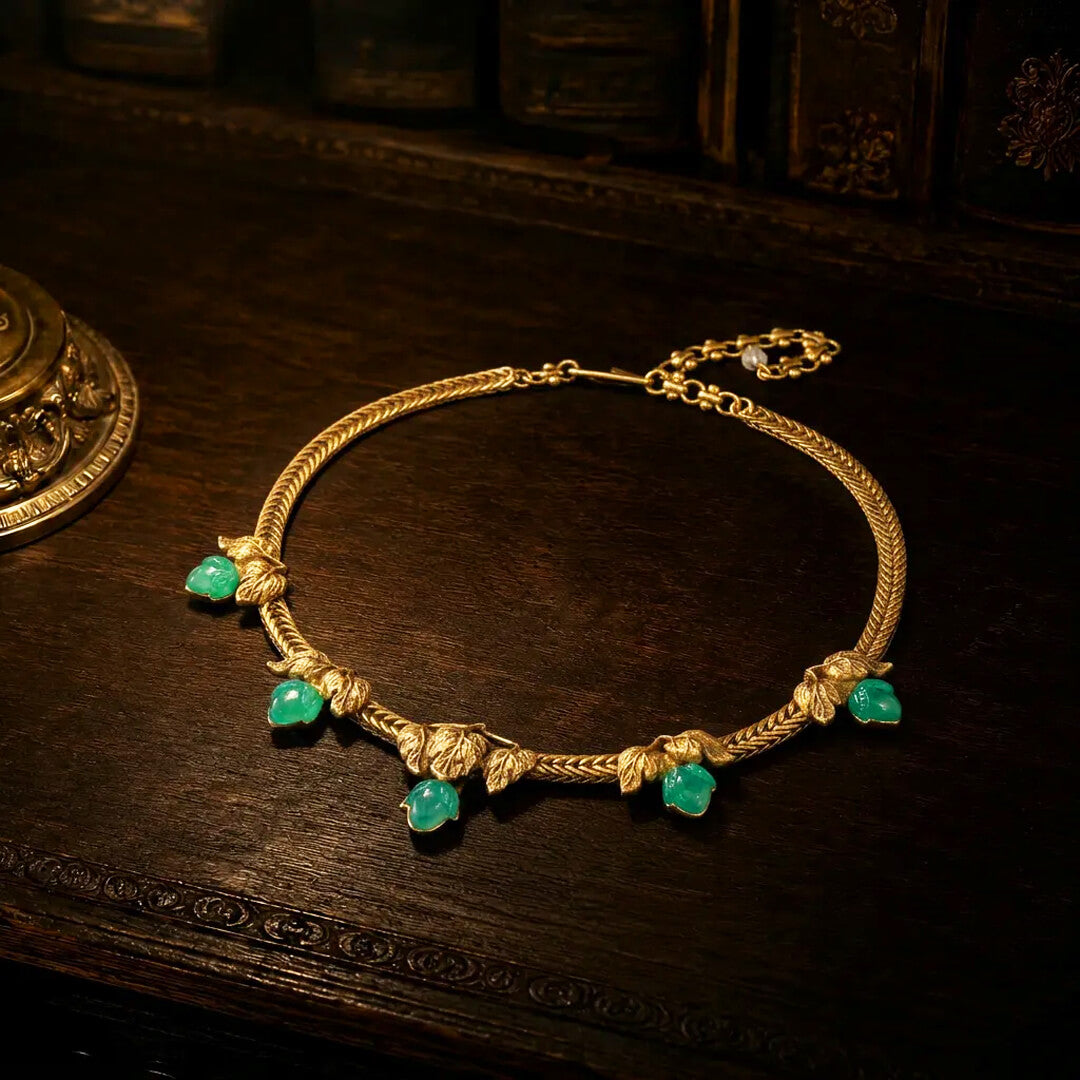 Vintage-inspired gold ivy leaf necklace with green resin stones resting on a dark wood antique desk.