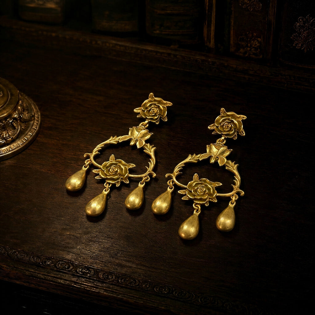 Flat lay view of heavy gold-tone chandelier earrings with rose motifs and teardrop dangles.
