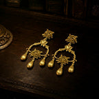 Flat lay view of heavy gold-tone chandelier earrings with rose motifs and teardrop dangles.
