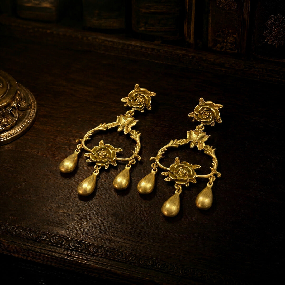 Flat lay view of heavy gold-tone chandelier earrings with rose motifs and teardrop dangles.