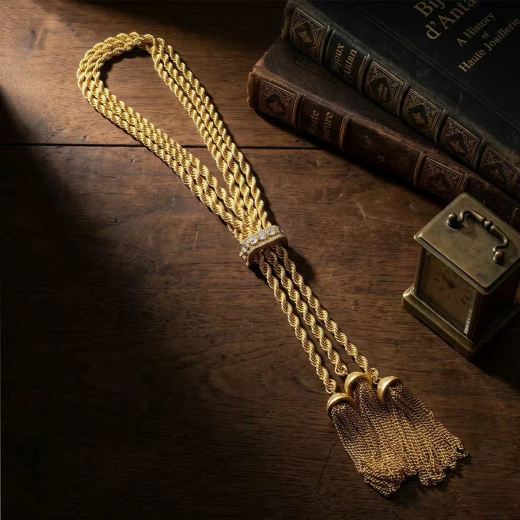 Vintage-inspired braided gold-tone lariat necklace resting on a dark antique wood table next to vintage books. Substantial heirloom piece for the dark academia aesthetic.