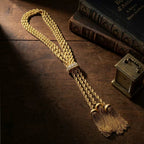 Vintage-inspired braided gold-tone lariat necklace resting on a dark antique wood table next to vintage books. Substantial heirloom piece for the dark academia aesthetic.