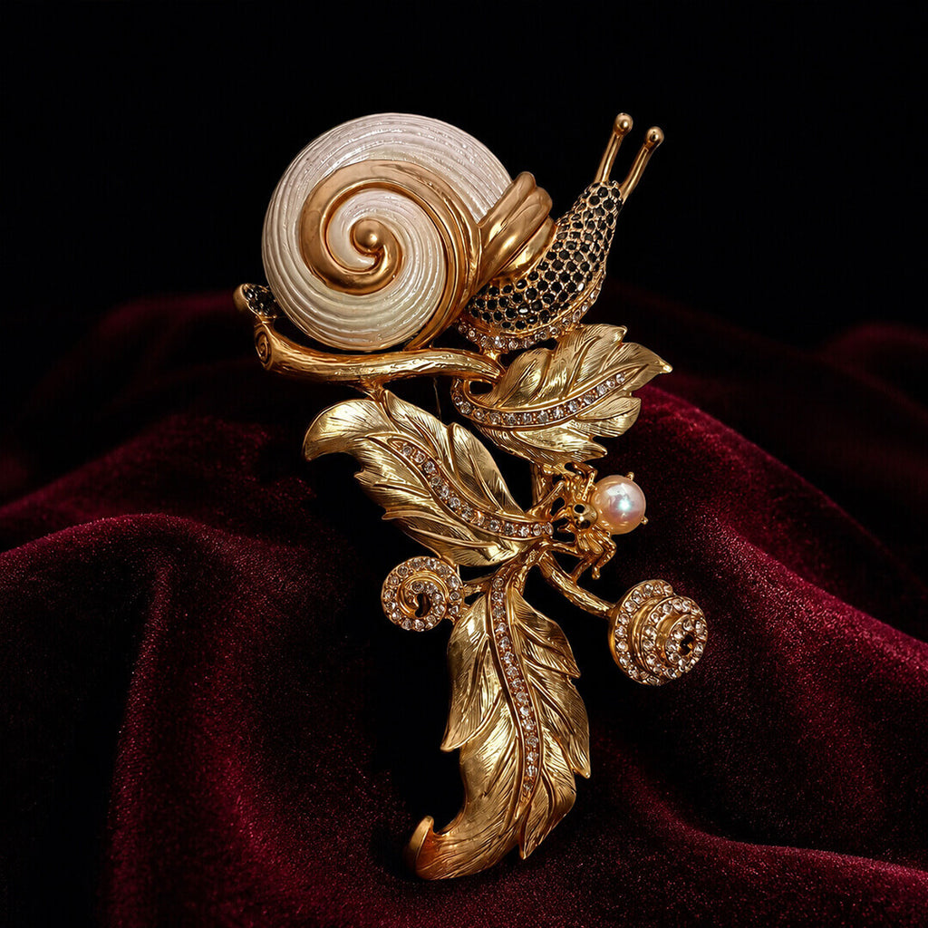 Intricate gold-tone snail and botanical leaf brooch displayed on rich burgundy velvet.
