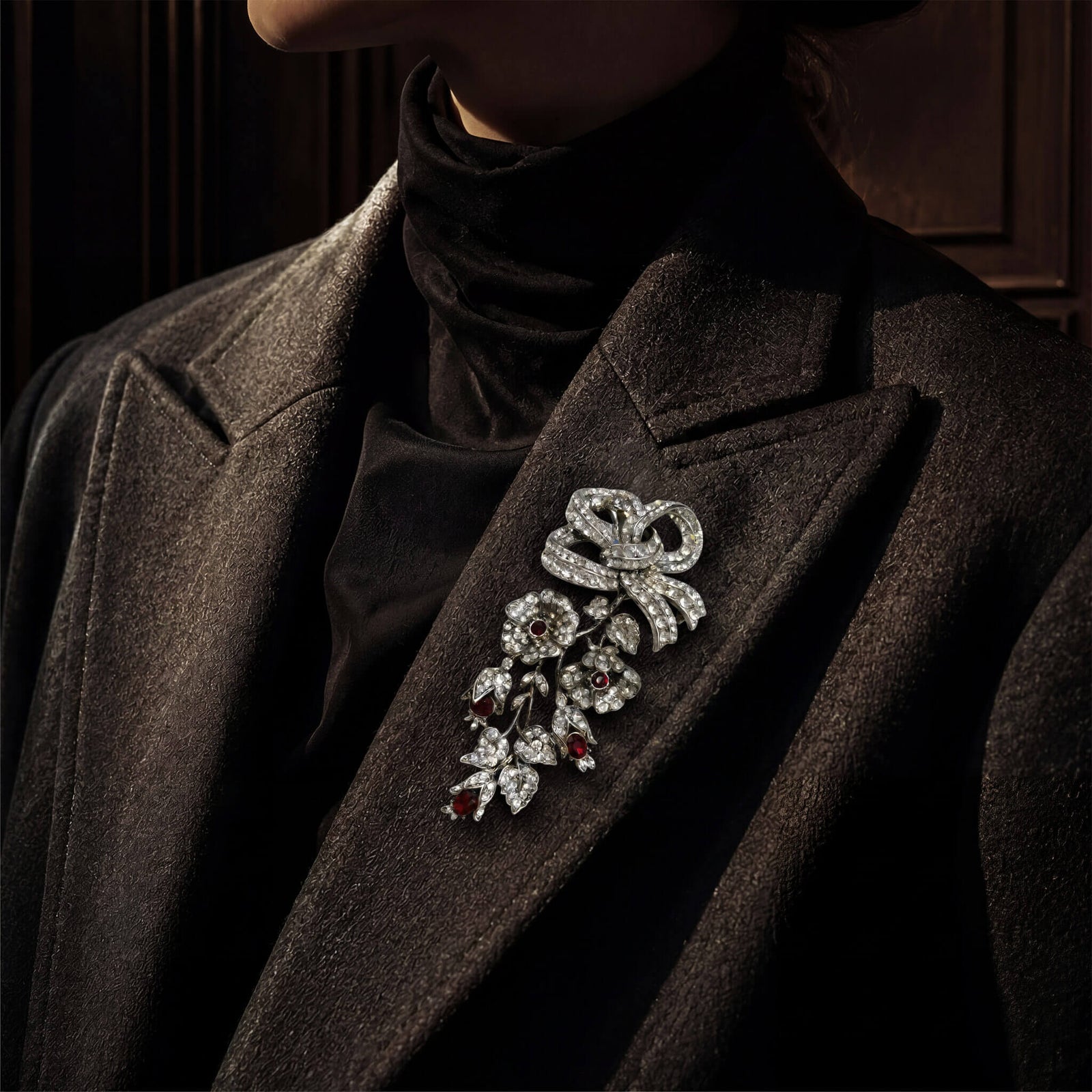 Close-up of the vintage-inspired silver and ruby-colored crystal floral cascading brooch pinned to a dark wool coat.