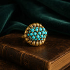 Vintage-Inspired turquoise cluster statement ring with a gold-tone setting on a dark vintage book.