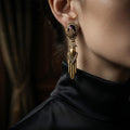 Woman wearing vintage-inspired heavy gold drop earrings with a purple amethyst cabochon, styled with a black silk turtleneck for a dark Old Money aesthetic.