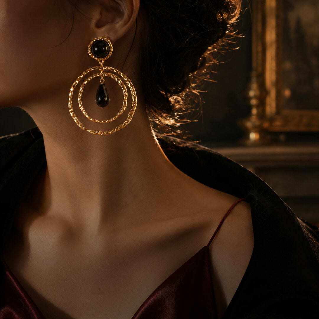 Woman wearing vintage-inspired hammered gold double hoop earrings with a black teardrop for an Old Money aesthetic.