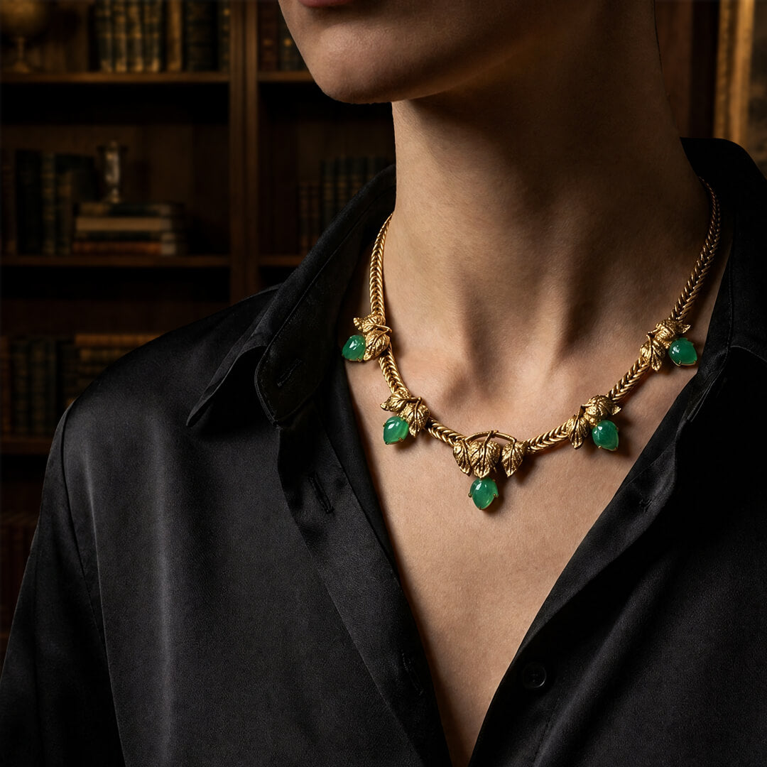 Woman wearing a vintage-inspired chunky gold collar necklace with green teardrop stones, styled with a black silk shirt in a dark academia library.