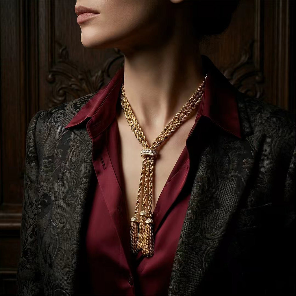 Model styled in a burgundy silk shirt wearing a retro style chunky gold lariat necklace with tassels. Curated statement jewelry for evening wear.