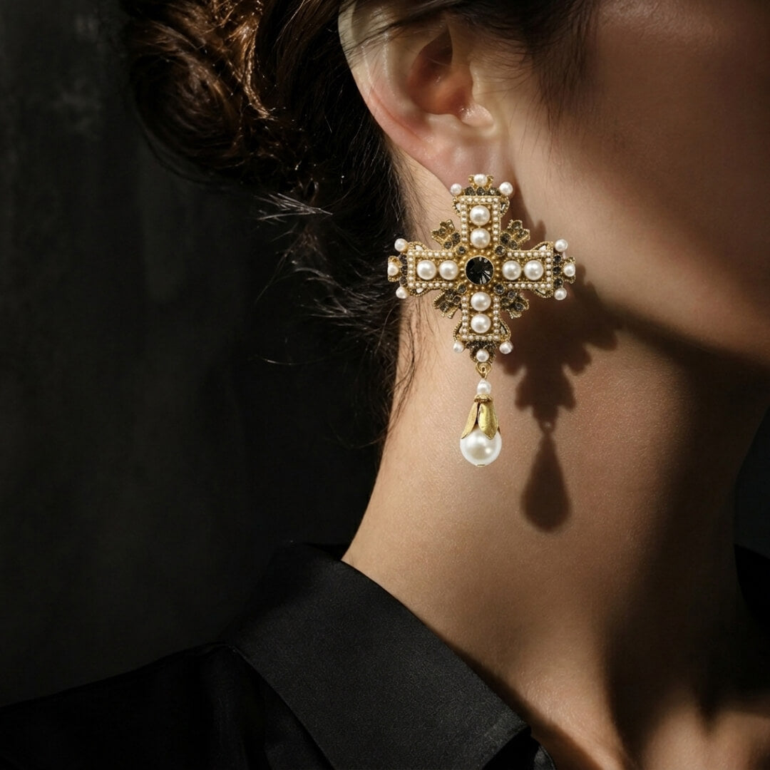 Close-up of vintage-style antiqued gold cross drop earrings featuring pearls and dark crystals.